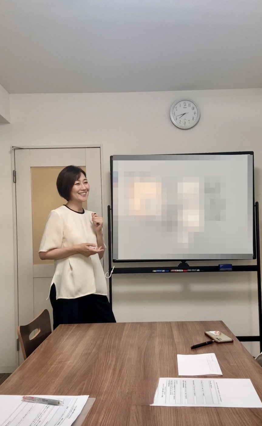 ホワイトボードの前で、笑顔で受講生に語りかける里実（Satomi）