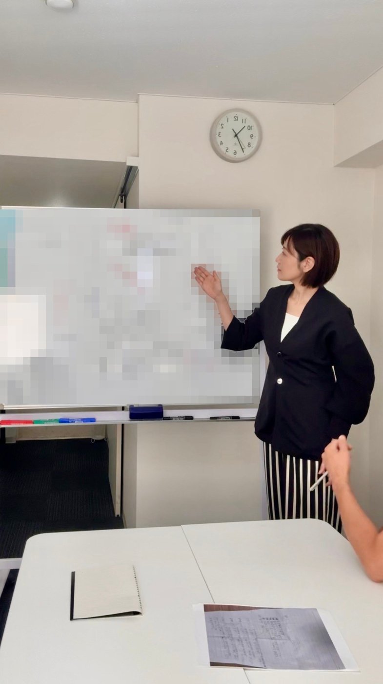ホワイトボードを指しながら講義をする里実（Satomi）